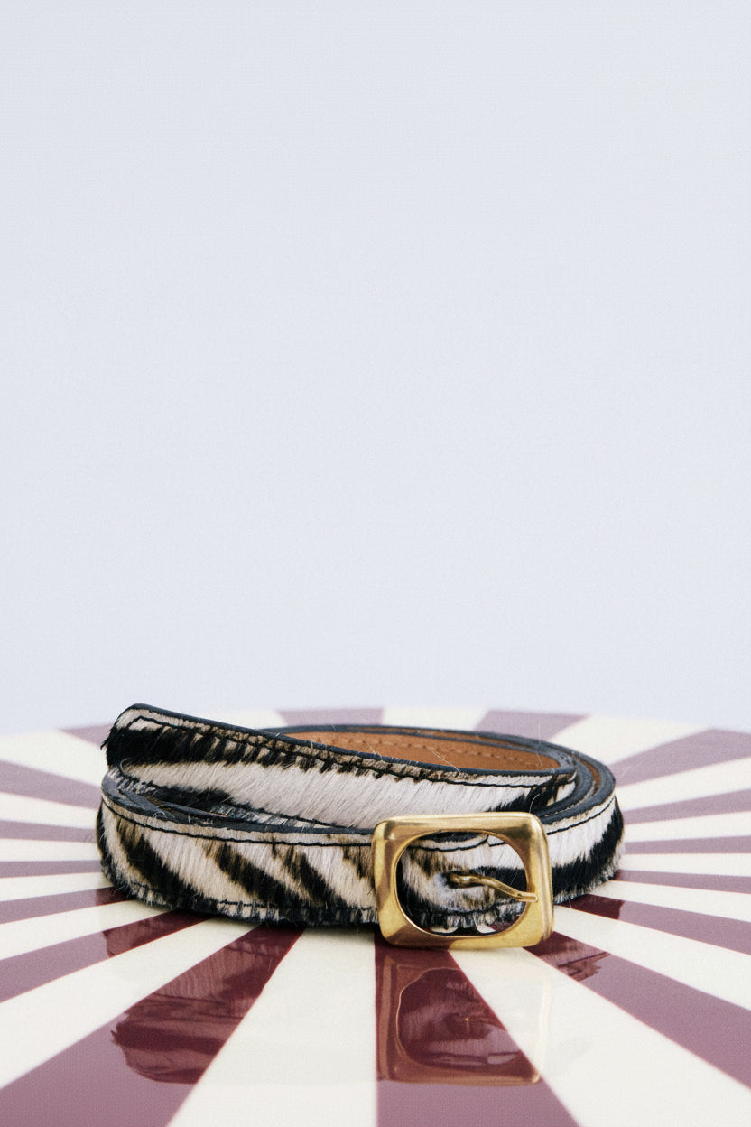 Zebra print belt with a gold buckle on a striped background